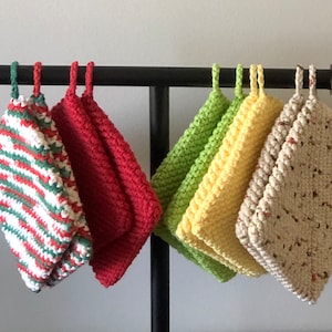 Può includere: Un set di 10 presine all'uncinetto appese a un rack di metallo nero. Le presine sono di vari colori, tra cui rosso, verde, giallo e beige.