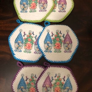 May include: Set of six crocheted pot holders with a gnome and hummingbird design. The pot holders are in three colors: green, blue, and purple.