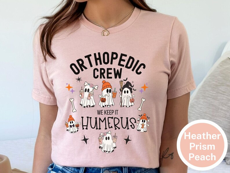 May include: A pink t-shirt with the text "Orthopedic Crew We Keep It Humerus" and a graphic of five ghosts holding drinks and sweets. The ghosts are wearing hats and have different facial expressions.