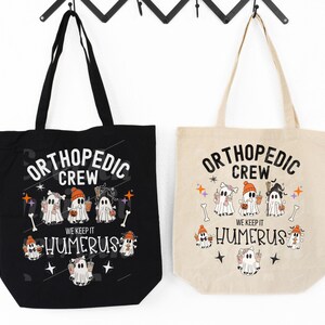 May include: Two black and beige tote bags with a Halloween theme. The bags feature a graphic of ghosts with the text "Orthopedic Crew" and "We Keep It Humerus".