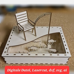 Puede incluir: Un modelo de madera de una escena de pesca con una silla, una caña de pescar y peces en un lago. El modelo está hecho de madera marrón claro y tiene un fondo blanco.