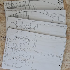 Peut inclure: Quatre feuilles de bois d&eacute;coup&eacute;es au laser avec des motifs pour un projet de bricolage. Les motifs comprennent un vase, des fleurs et un &eacute;l&eacute;ment d&eacute;coratif. Le bois est brun clair et les motifs sont noirs.