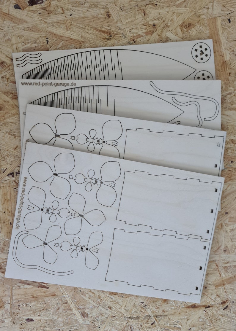 Peut inclure: Quatre feuilles de bois d&eacute;coup&eacute;es au laser avec des motifs pour un projet de bricolage. Les motifs comprennent un vase, des fleurs et un &eacute;l&eacute;ment d&eacute;coratif. Le bois est brun clair et les motifs sont noirs.