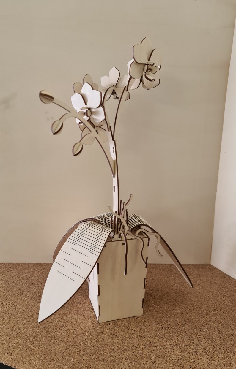 Peut inclure: Une sculpture d'orchid&eacute;e en bois avec trois fleurs et un pot. La sculpture est en bois d&eacute;coup&eacute; au laser et a une finition en bois naturel.