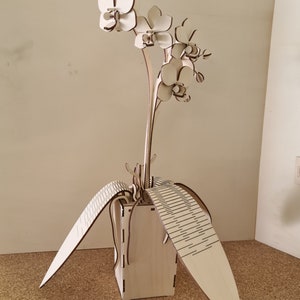 Peut inclure: Une sculpture d'orchid&eacute;e en bois avec trois fleurs blanches et des feuilles. La sculpture est dans un pot en bois avec un motif d&eacute;coratif.