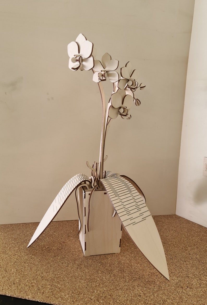 Peut inclure: Une sculpture d'orchid&eacute;e en bois avec trois fleurs blanches et des feuilles. La sculpture est dans un pot en bois avec un motif d&eacute;coratif.