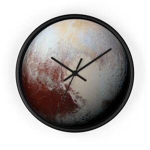 May include: A black framed wall clock with a detailed image of Pluto, a dwarf planet in our solar system. The clock face features a brown, white, and gray surface with a black clock hand.
