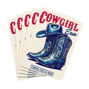 May include: Playing cards featuring a blue cowboy hat and boots design with the words "COWGIRL Era" in red and blue. The phrase "COWGIRL STATE OF MIND" is also present. The cards have a cream background.