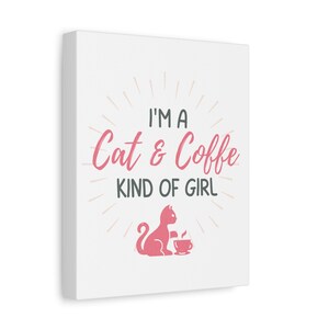 Op de afbeelding: Witte canvas print met de tekst "I'M A Cat & Coffee KIND OF GIRL" in roze en grijs. Een roze katten silhouet zit naast een koffiekopje. Het ontwerp is omgeven door roze zonnestralen.