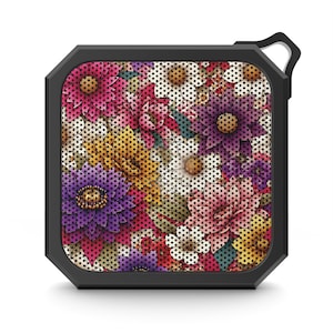 May include: A small black portable Bluetooth speaker with a floral design. The speaker has a textured, patterned surface with a variety of colorful flowers.