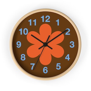 May include: Circular wall clock with a brown face, an orange flower design, and blue numerals. The clock has black hands and a light wood frame. A decorative clock, measuring approximately 25 cm in diameter.