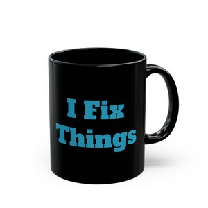 May include: Black ceramic coffee mug with a white handle. The mug has blue text that reads "I Fix Things".