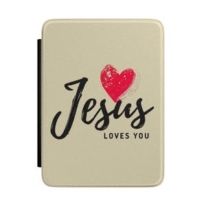 May include: A rectangular beige tablet or e-reader case with a textured surface. The front features the black script text Jesus and the block text LOVES YOU, accompanied by a red heart graphic with a white speckled paint splatter effect.
