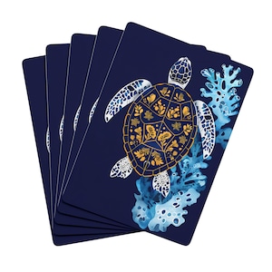May include: Navy blue playing cards featuring a sea turtle design. The turtle has a gold and floral patterned shell, white flippers, and is surrounded by blue coral. The cards are fanned out, showing the design on the front.