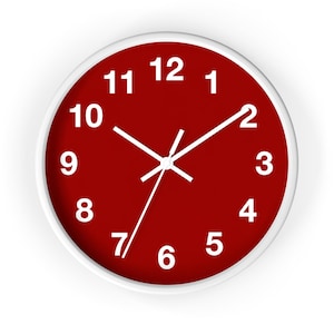 May include: A round wall clock featuring a deep red face with bold white Arabic numerals from one to twelve. The clock has a simple white frame and three thin white hands indicating the hour, minute, and second, providing a clear display.