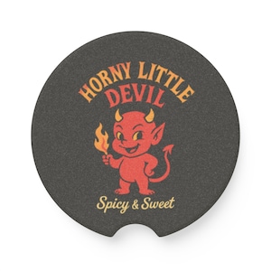 May include: Black round car coaster with a cartoon devil illustration. The red devil holds a flame and has yellow horns. Text reads "Horny Little Devil" above the image and "Spicy & Sweet" below.