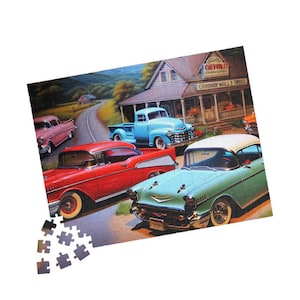 May include: A jigsaw puzzle depicting a vintage scene with classic cars parked outside a Chevrolet dealership. The puzzle includes a red car, a blue pickup truck, and a green car. The dealership sign reads "Chevrolet".