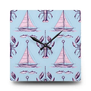 Puede incluir: Reloj de pared cuadrado con un fondo azul claro que presenta un patrón repetido de veleros con velas rosas, langostas y peces. Las manecillas del reloj son negras.