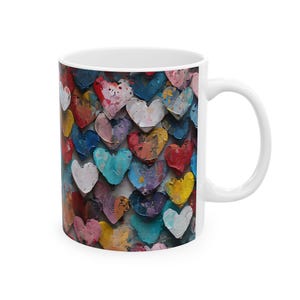 May include: White ceramic mug with a colourful heart design. The hearts are painted in various colours, including red, blue, yellow, and pink, creating a vibrant and artistic look. The mug has a standard handle and a glossy finish.