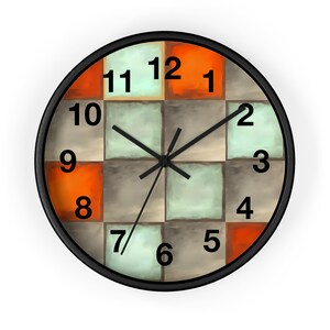 May include: A round wall clock with a black frame. The clock face features a checkerboard pattern in orange, light green, and gray squares. Black hands indicate the time, with the numbers 1 through 12 in a black, sans-serif font.
