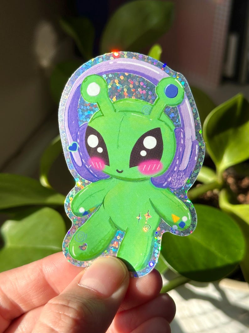 Puede incluir: Un extraterrestre verde con ojos grandes y una diadema morada con un acento azul. El extraterrestre lleva auriculares y tiene un fondo hologr&aacute;fico brillante.