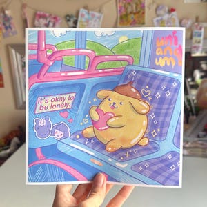 May include: A yellow cartoon dog with a brown hat holds a pink heart in a blue and purple checkered seat on a bus. The text "it's okay to be lonely" is on a sticker on the seat in front of the dog. The text "uni and uni" is in the upper right corner of the image.