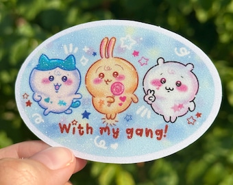 Könnte beinhalten: Ovaler Aufkleber mit drei niedlichen Cartoon-Charakteren auf hellblauem Hintergrund mit Glitzer. Der Aufkleber trägt die Aufschrift "With my gang!". Die Charaktere sind eine Katze, ein Hase und ein Bär, alle im Kawaii-Stil gestaltet.