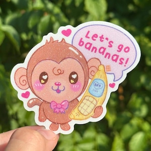 Puede incluir: Una pegatina con un mono de dibujos animados con un lazo rosa, sosteniendo un plátano con "BFF Call". Un bocadillo dice "Let's go bananas!" con corazones rosas. La pegatina tiene un efecto brillante.