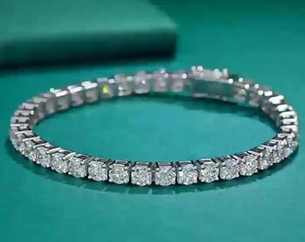 May include: A silver bracelet with numerous square-cut, clear gemstones. The bracelet is set on a teal-colored surface, with a matching background. The gemstones are evenly spaced and reflect light.