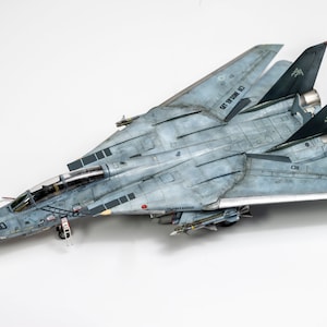 Op de afbeelding: Een grijs en wit model van een straaljager met de tekst "GET OFF MY 6" aan de zijkant. De straaljager heeft een schedel en gekruiste beenderen op de staart.
