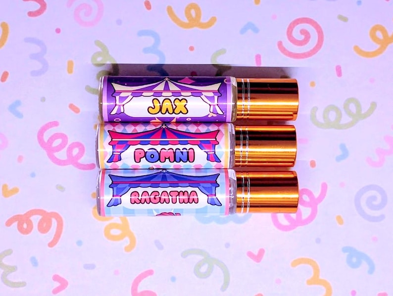 May include: Three perfume roller bottles with gold caps. Each bottle has a label with a circus tent design and a name: Jax, Pomni, and Ragatha. The background is a light purple with colourful confetti.