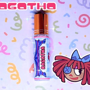 May include: A perfume roll-on bottle with a copper cap and a label reading "RAGATHA" in pink. The label features a blue and white checkered pattern and a cartoon doll illustration. The background is light purple with colourful swirls.