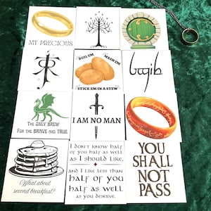 May include: A collection of square cards with illustrations and text from a fantasy series. The cards feature images of a gold ring, a tree, a green door, and other themed graphics. A gold ring on a chain is also present.