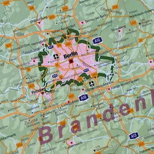 May include: A map of Brandenburg, Germany, with the city of Berlin highlighted in pink. The map shows major roads, cities, and towns in the region. The word "Brandenburg" is written in large, bold letters across the bottom of the map.