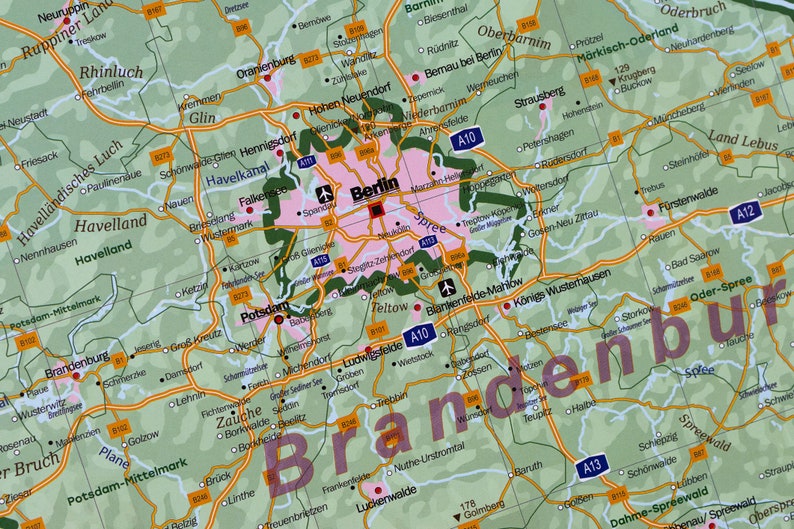 May include: A map of Brandenburg, Germany, with the city of Berlin highlighted in pink. The map shows major roads, cities, and towns in the region. The word "Brandenburg" is written in large, bold letters across the bottom of the map.