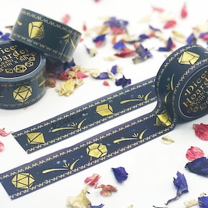 May include: Two rolls of dark blue washi tape with gold foil accents. The tape features a repeating pattern of dice and stars. The tape is labeled "Dice Hoarder Washi Tape 2cm x 12m".