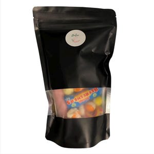 May include: A black, resealable bag with a clear window displaying colorful candies. The bag has a white sticker with the word "Dolce" and a chili pepper illustration. The candy package includes the word "Refreshers".