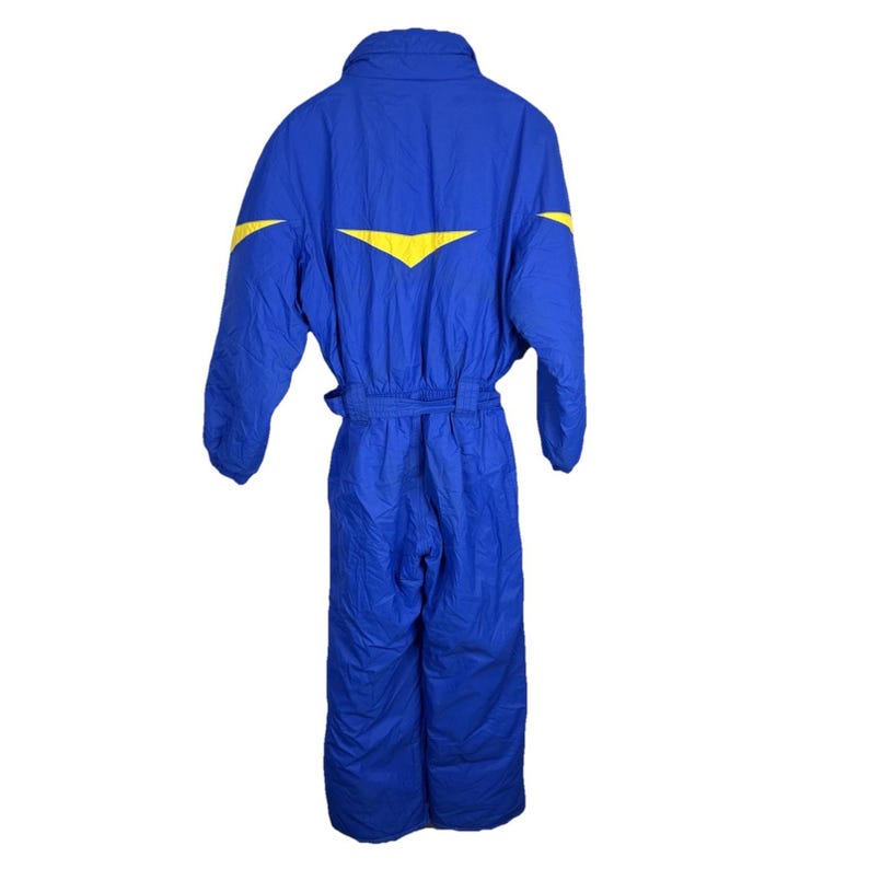 May include: A blue one-piece snowsuit with yellow chevron accents on the shoulders. The snowsuit has a belted waist and a collar. The snowsuit is made of a quilted material.