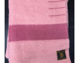 Peut inclure: Une couverture rose pliée avec une bande rose plus foncée au milieu. La couverture a un aspect texturé et une petite étiquette rectangulaire dans le coin inférieur droit. L'étiquette a des lettres dorées et un logo.