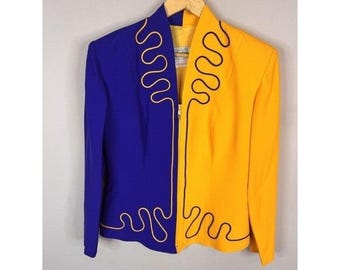 May include: A two-toned jacket, half royal blue and half yellow, hangs on a wooden hanger. The jacket features a zipper closure and a unique design with black squiggly lines. The jacket is a bold statement piece.