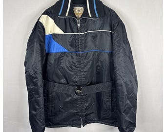 Peut inclure: Veste de ski vintage noire avec un motif color block blanc, bleu et noir. La veste a une fermeture éclair sur le devant, une ceinture et le mot "Montreal" sur le col.