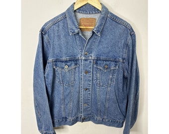 Peut inclure: Une veste en jean bleu clair avec une fermeture à boutons, deux poches poitrine et deux poches avant. La veste a une étiquette de marque Levi's sur la poche poitrine gauche.