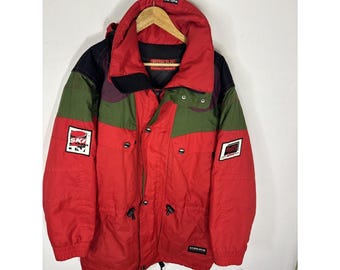 Peut inclure: Veste de ski vintage rouge, verte, noire et violette avec capuche. La veste présente plusieurs écussons, une taille ajustable par cordon de serrage et la marque "SUNICE". Suspendue à un cintre en bois.