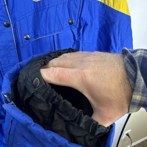 May include: Blue and yellow ski jacket with black detailing. The jacket has a zip front, snap fastenings, and a pocket. The interior lining is black. The jacket is made of a durable, water-resistant material.