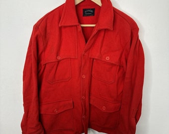 May include: A red wool jacket with a button-up front and multiple pockets. The jacket has a label that reads "Pioneer Garment Co."