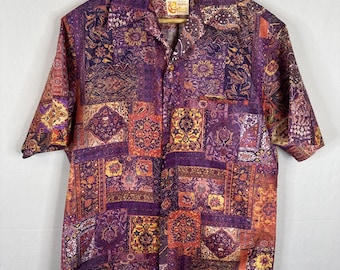 May include: Short-sleeved button-down shirt with a patchwork design in shades of purple, orange, and gold. The shirt features a collared neckline and a single chest pocket. The fabric has a detailed, ornate pattern.