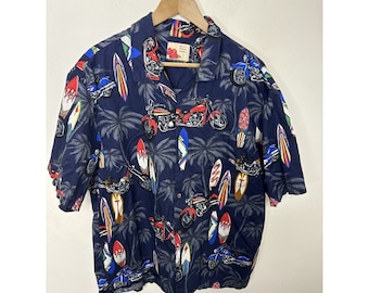 May include: A blue short-sleeved button-down shirt with a tropical print featuring motorcycles, palm trees, and surfboards. The shirt has a white tag with the text "Bali" and "Paradise".