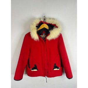 Peut inclure: Une veste rouge vif dotée d'une capuche avec une épaisse bordure en fausse fourrure crème. La veste présente des manches longues, une fermeture éclair frontale et deux poches avant, chacune ornée d'un appliqué graphique de phoque noir et blanc.
