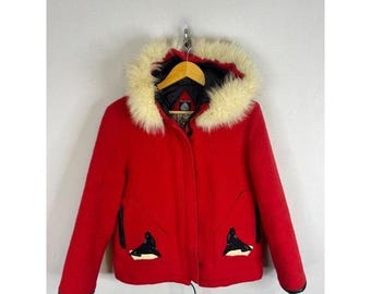 Peut inclure: Une veste rouge vif dotée d'une capuche avec une épaisse bordure en fausse fourrure crème. La veste présente des manches longues, une fermeture éclair frontale et deux poches avant, chacune ornée d'un appliqué graphique de phoque noir et blanc.