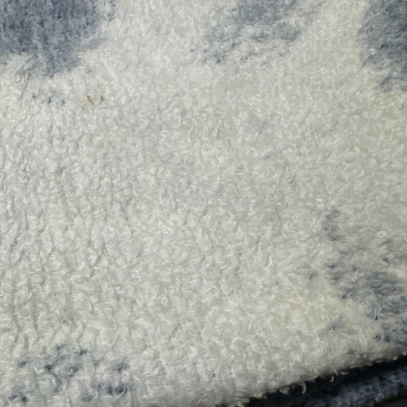 Puede incluir: Primer plano de una tela suave y texturizada con una base blanca y un patr&oacute;n de te&ntilde;ido anudado azul. El material parece afelpado y esponjoso, con un pelo denso y rizado. La tela tiene un aspecto acogedor y acogedor.